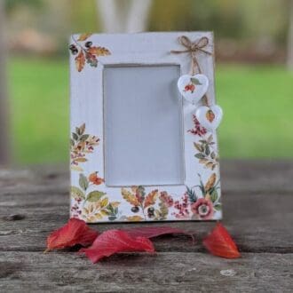 White washed 6 x 4 wooden frame decoupaged with an Autumn leaves design and finished with two white hearts hanging from natural twine.