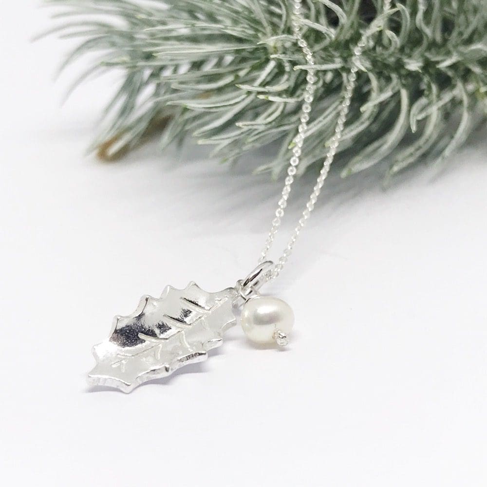 silver holly leaf necklace with a freshwater pearl on a white background with snow covered pine needles