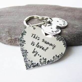 A heart shaped aluminium keyring hand stamped with 'this mummy is loved by' with personalised name discs.