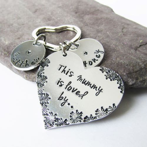 A heart shaped aluminium keyring hand stamped with 'this mummy is loved by' with personalised name discs.
