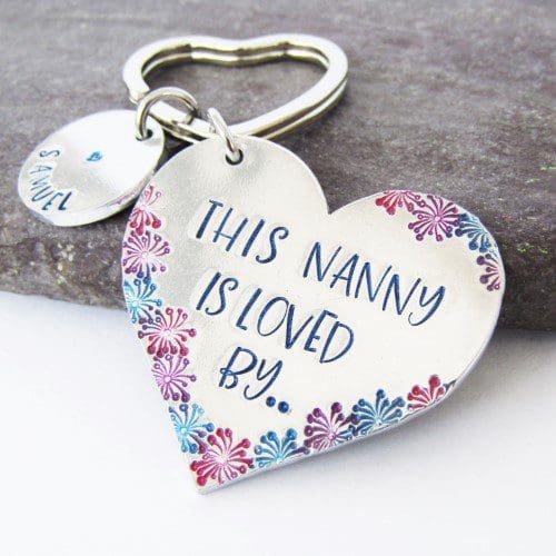 aluminium heart keyring hand-stamped with 'this Nanny is loved by' coloured blue with coloured flower details and blue lettered personalised name tags
