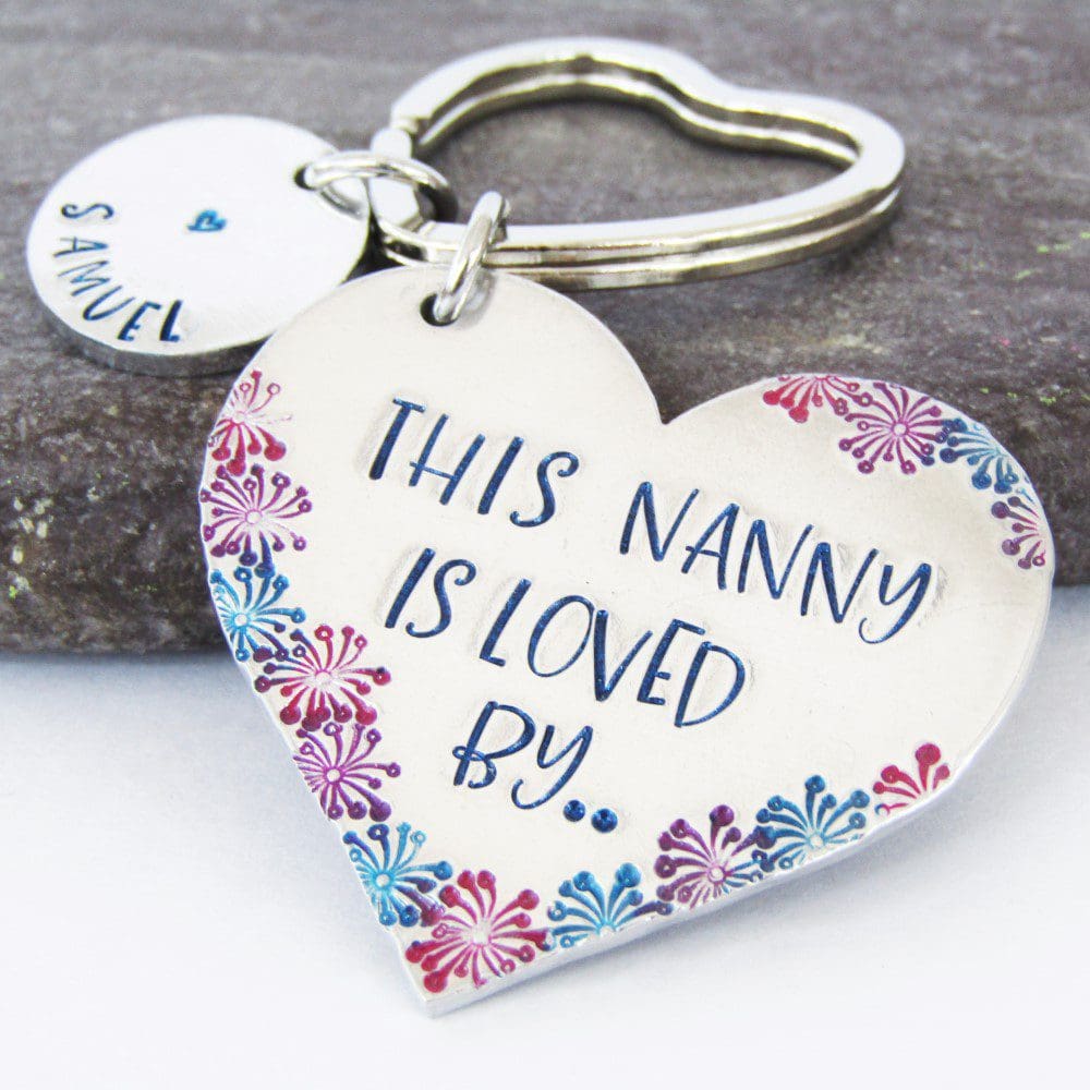 aluminium heart keyring hand-stamped with 'this Nanny is loved by' coloured blue with coloured flower details and blue lettered personalised name tags