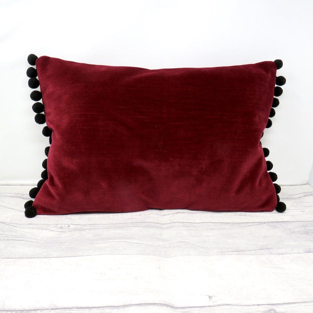 Handmade rectangular cushion in burgundy velvet with a black pompom trim.