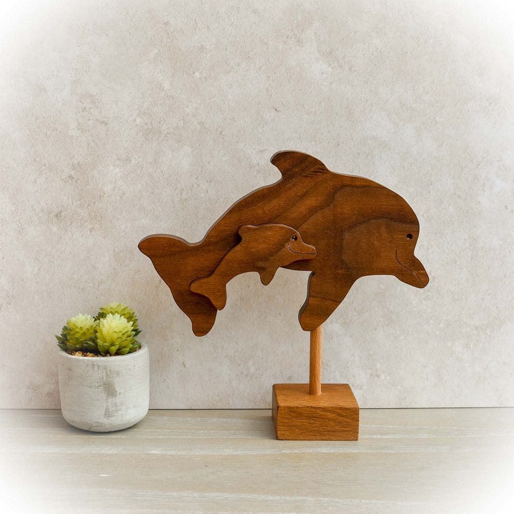 Two interlocking jumping dolphins, handmade and cut from dark wood using a scroll saw and set onto a lighter wood base.