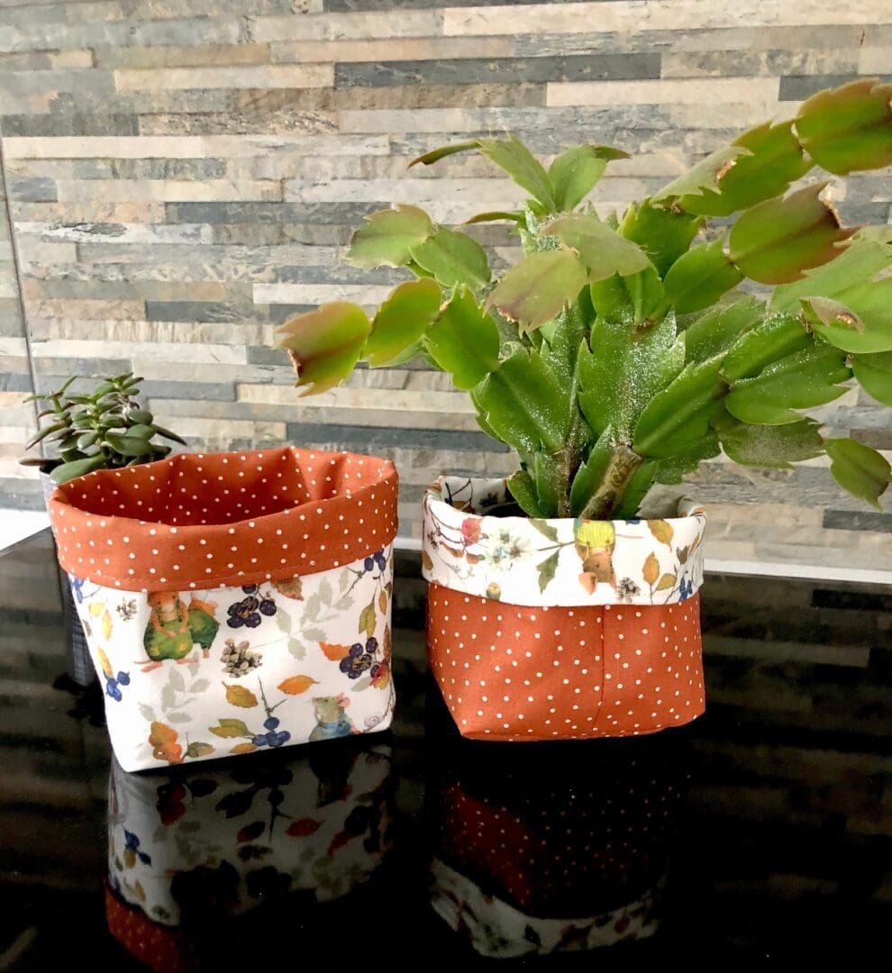 Reversible fabric pots in brown spot fabric and autumn mice fabric with a small plant on a brick background