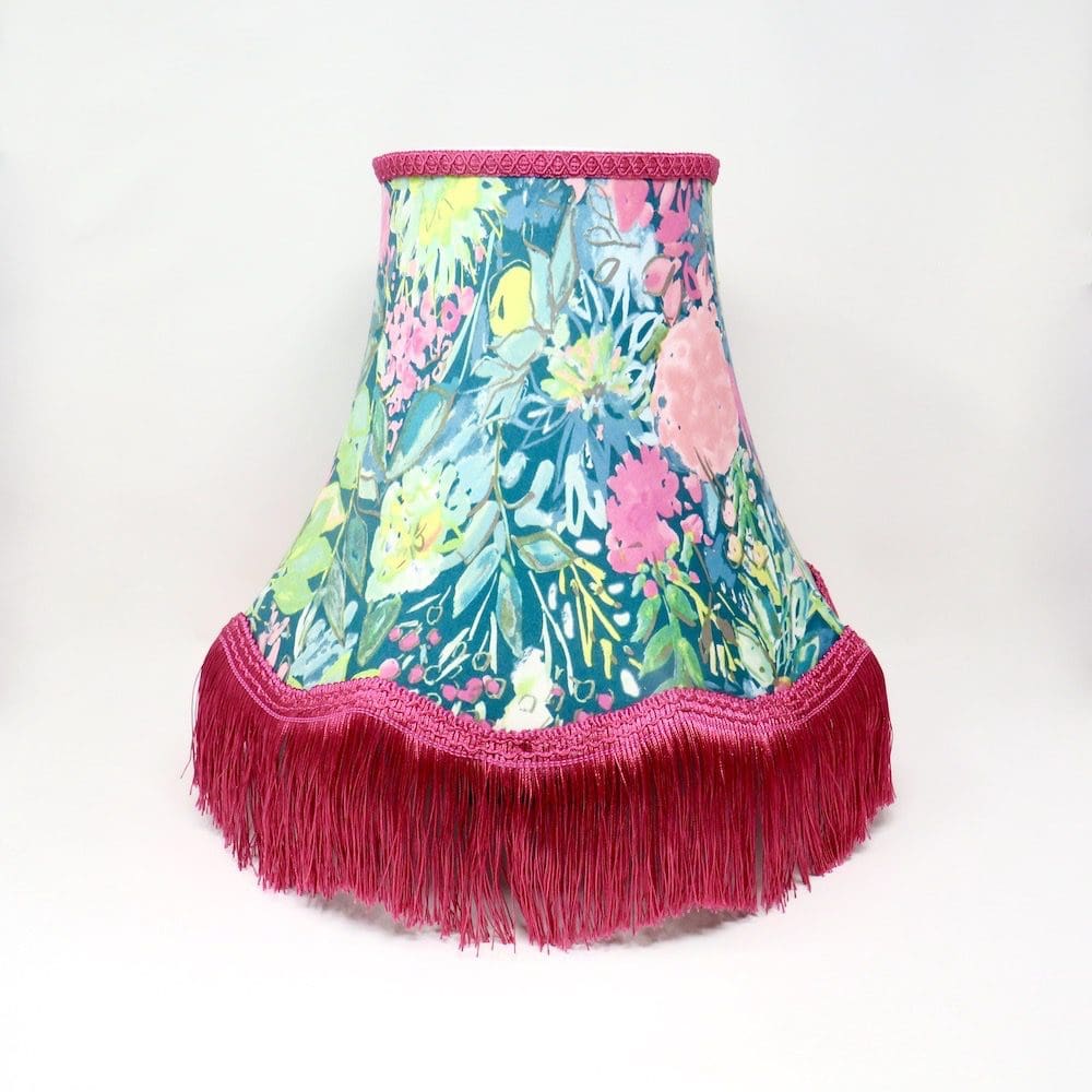 A traditionally made lampshade in a pink and green floral print with a long pink fringe trim.