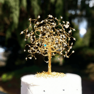 Gold wire tree cake topper decorated with crystals and birthstones on the branches sitting on top of a wedding cake.