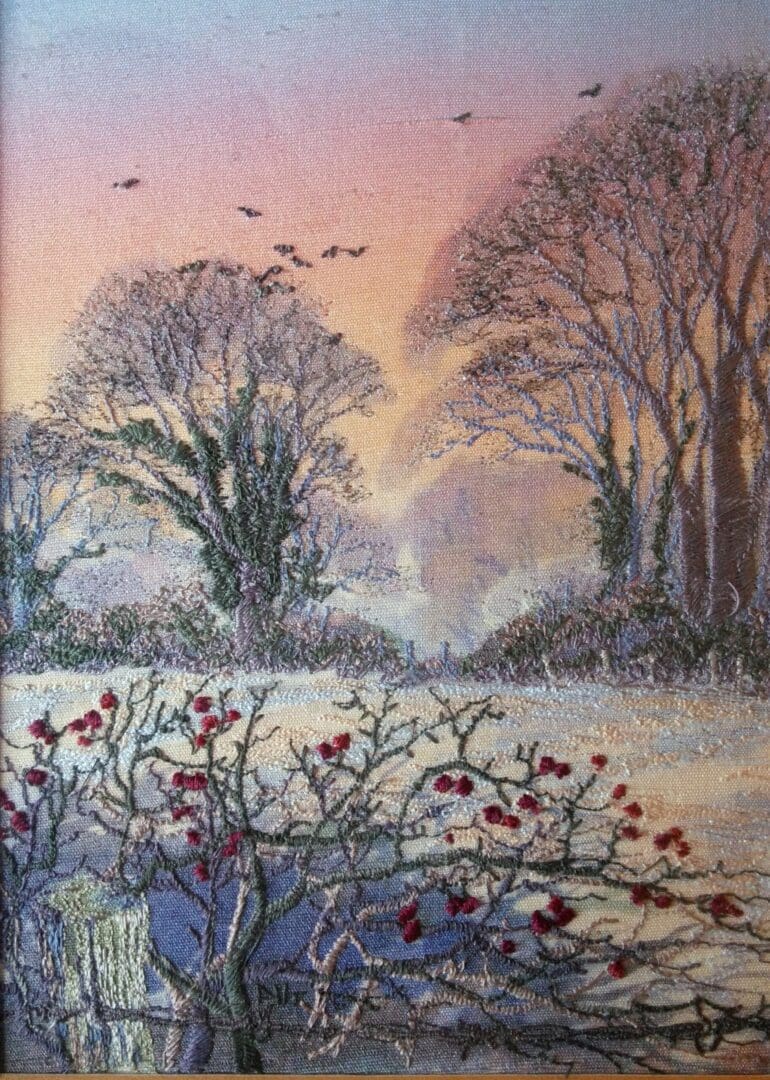 A machine embroidered Thread Painting of Hawtrhorn berries in a hedge looking across a field to winter trees with late evening glow in the sky around November and feels misty and coldter tree 
