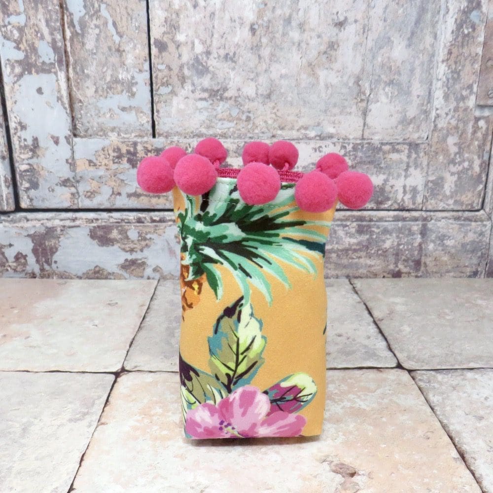 A mini velvet storage pot in a yellow pineapple print and with a cerise pom pom trim.