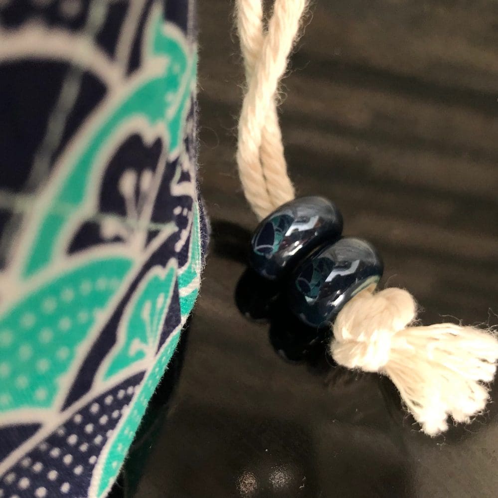 Close up view of the chunky shiny blue beads on a mini drawstring bag in stylistic Japanese wave design in blue and teal with pale green lining, standing on a black surface