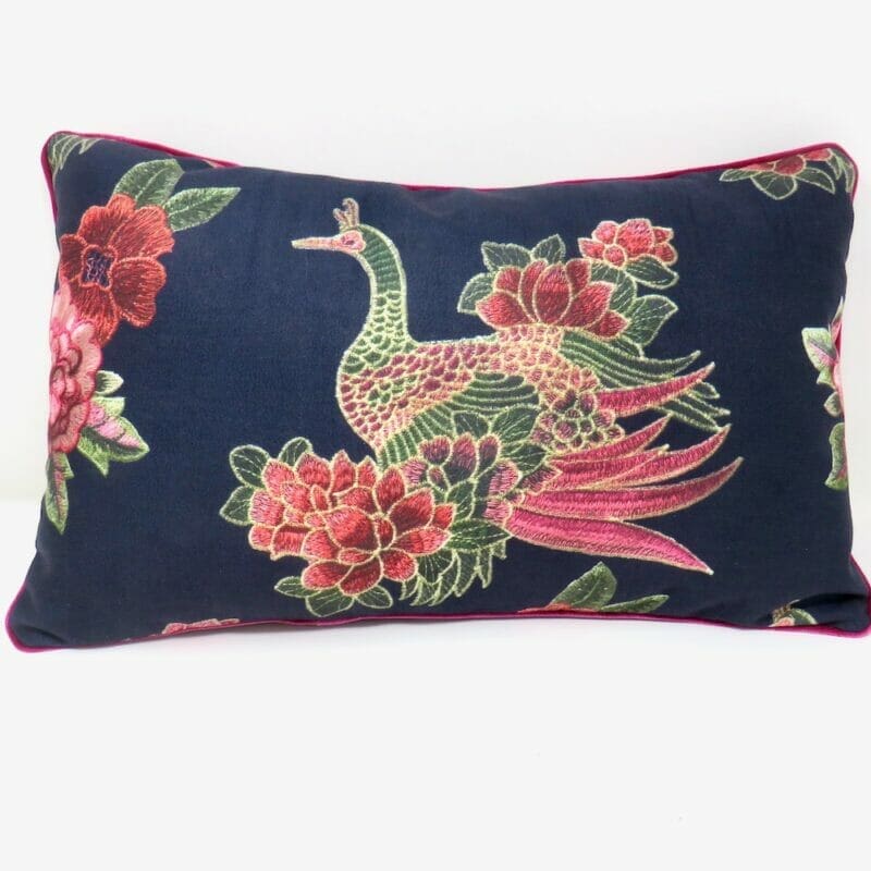 A black peacock print velvet cushion with pink piped edges.