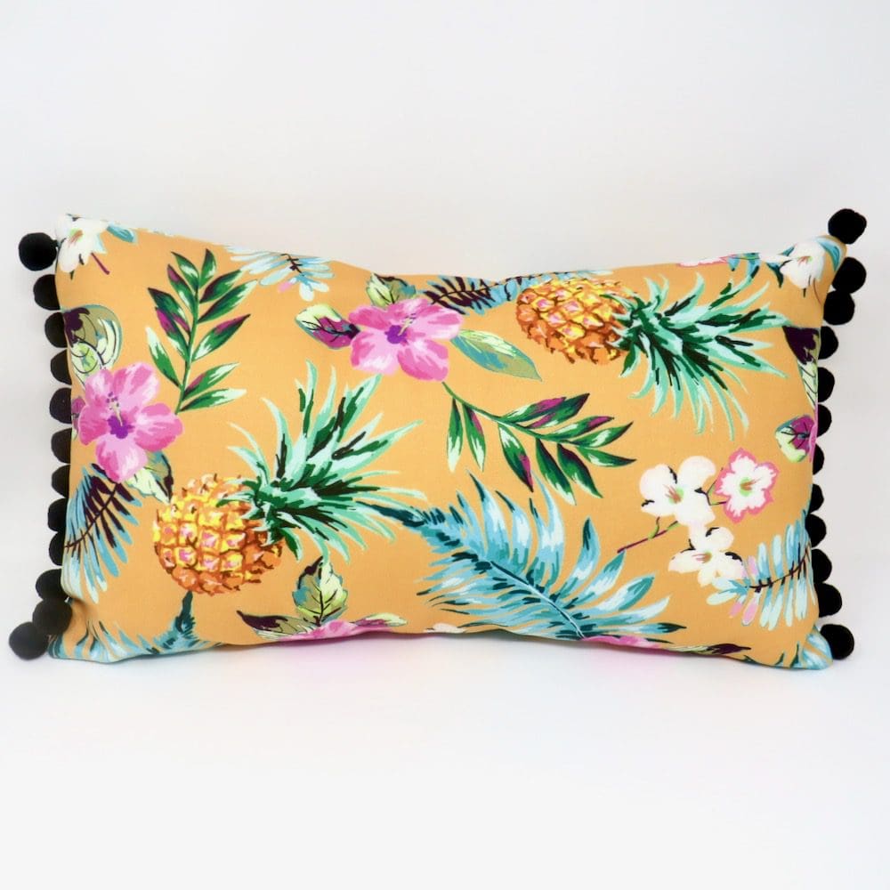 A handmade boudoir style cushion in a yellow pineapple print velvet with a black pom pom