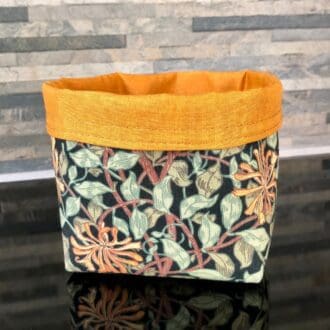 Reversible fabric organiser in William Morris Honeysuckle design on a black background and rich ochre yellow. Standing on a shiny black surface.