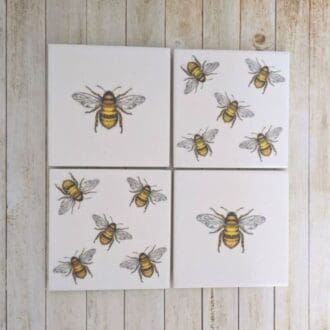 Set of 4 white ceramic coasters decoupaged with a bee design, two with a single bee and 2 with 5 bees.