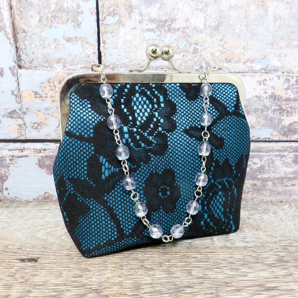 A compact teal and black lace evening bag with a beaded handle