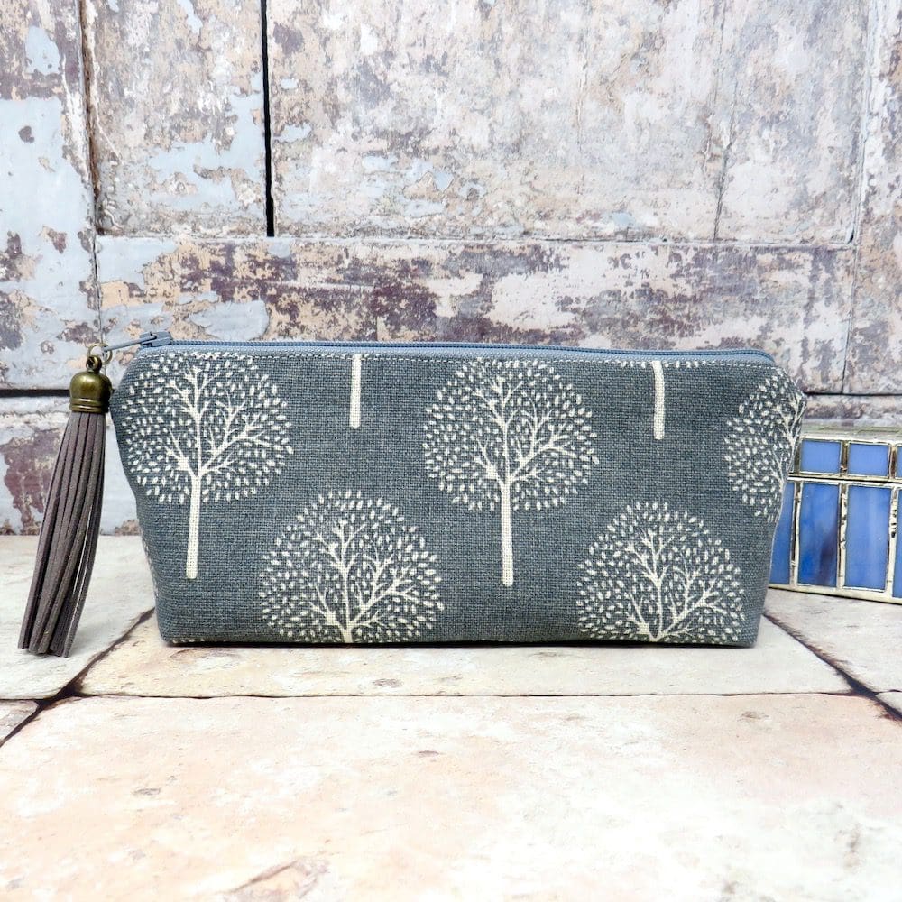 A zipped pouch handmade in a blue grey tree print cotton and with a fauz suede tassel trim.