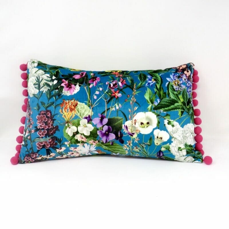 A turquoise floral velvet boudoir style cushion with a cerise pom pom trim.