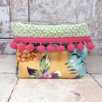 Velvet storage tub in a yellow pineapple print and with a cerise pom pom trim.