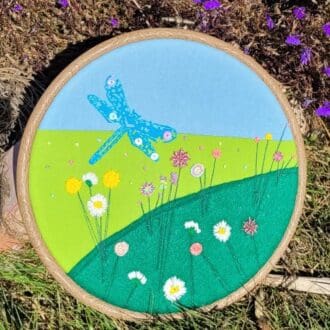 Hand embroidered 8 inch hoop of a dragonfly flying amongst flowers.