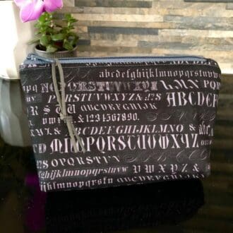 A charcoal grey zipped bag in pale grey old fashioned typeface fabric with pink orchid in background
