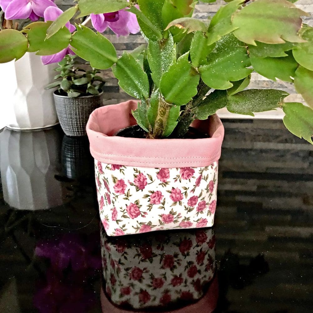 Reversible fabric pot in pink and white floral fabric with pale pink lining, used as a flower pot holder standing on a reflective black surface