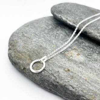 minimalist silver circle pendant on a silver chain draped over grey slate stone on a white background