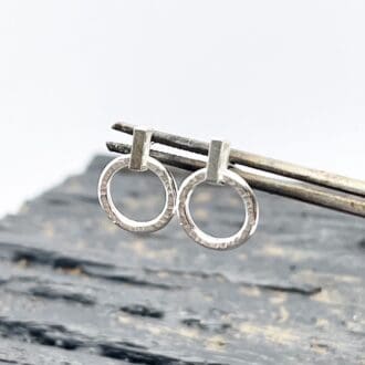 silver circle drop earrings being held up by a pair of tweezers over a grey background