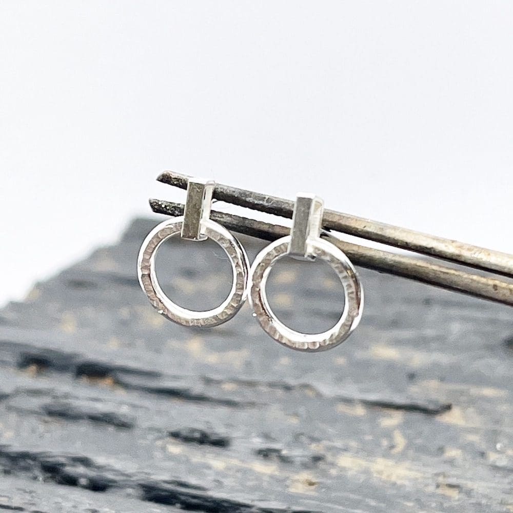 silver circle drop earrings being held up by a pair of tweezers over a grey background