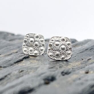 silver earrings embossed with the texture of a sea urchin shell on a grey background