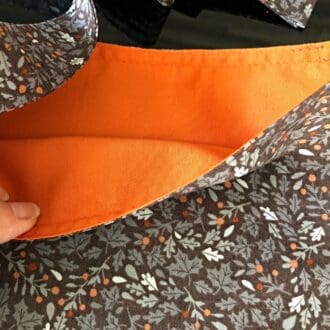 Adjustable cross body style mastectomy drain bag in Makower's leaves and bright orange lining, on a shiny black surface