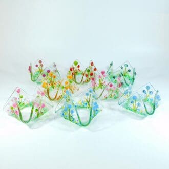 A collection of glass tealight holders decorated with glass dots, frit and stringers to show a floral meadow scene