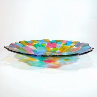 A large fused glass bowl made with a multitude of square coloured glass pieces overlapping each other.