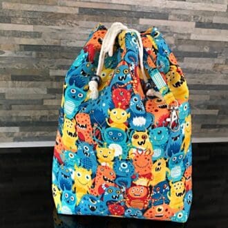 A large drawstring bag using Makower's Cute and colourful Aliens. With a bright yellow lining, cotton cord and shiny blue chunky beads. An integral swivel hook for use as a stitch holder or key fob.
