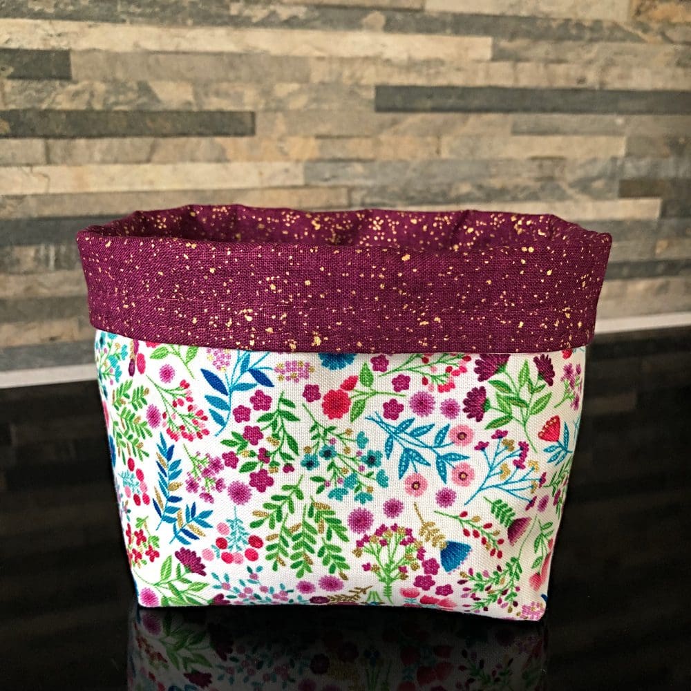 A reversible fabric pot in Makower's stunning Jaipur Floral range with an aubergine purple lining and metallic gold flecks, standing on a reflective black surface