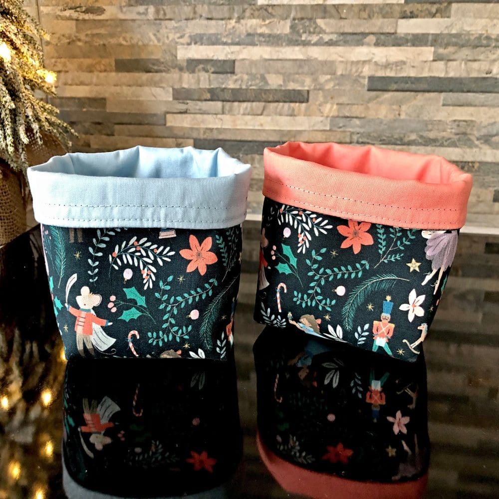 Reversible fabric pots in a delightful Christmas theme with images of the Nutcracker ballet fabric with either a pale blue or warm salmon reverse lining, standing on a reflective black surface