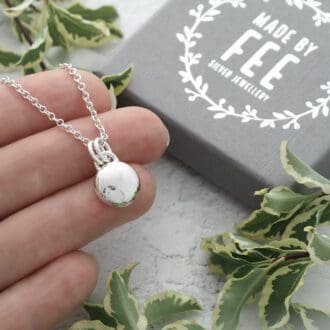 13.5mm diameter argentium sterling silver round pebble pendant with u-shaped bail and double jump rings on an argentium trace chain shown on hand for size reference