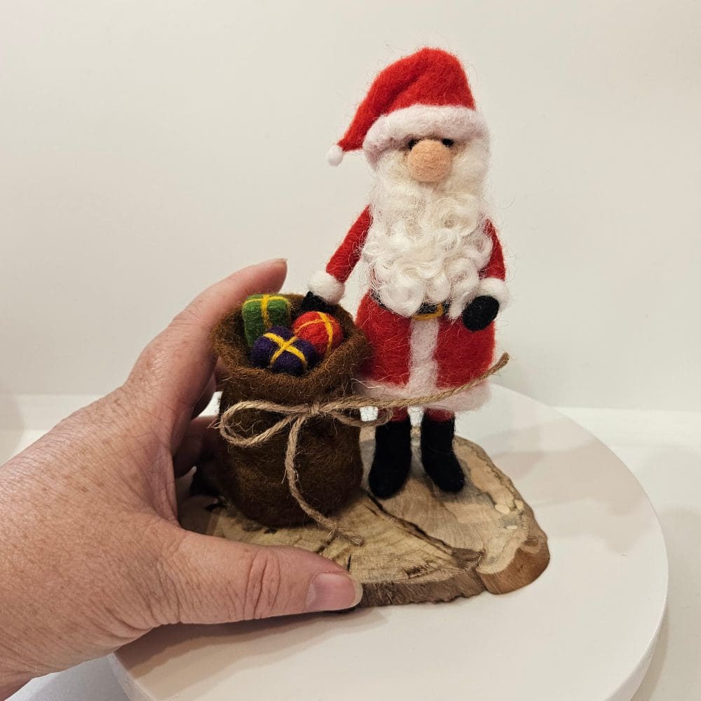Hand holding a needle felted Santa figurine with sack of presents.