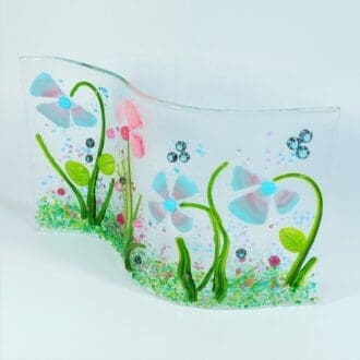 A fused glass floral scene in a gentle curve so that it stands up on it's own. Pretty pinks and blues with green stems and colourful dots to match.