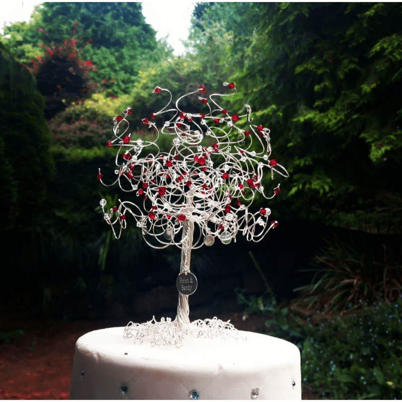silver tree cake topper with ruby crystals and silver charms sitting on a cake