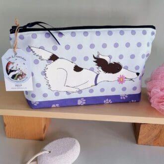 A large cotton handmade washbag featuring a background of pale purple spots, paw prints on the base and a brown and white scruffy dog running across the front of the bag with a pink flower in it's mouth.