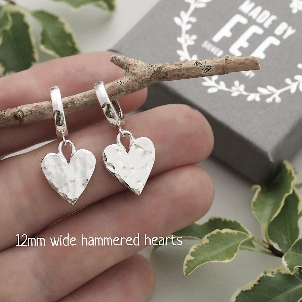 12mm wide sterling silver hammered hearts suspended from 12mm diameter sterling silver leverback hoop earrings shown on hand for size