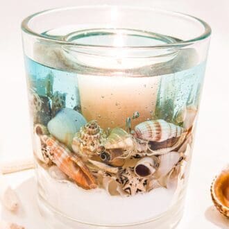 Blue sea ocean scented soy and gel wax candle sits on a white background with shells