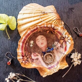 Gilded decoupage scallop shell trinket jewellery dish featuring Klimt's Portrait Of A Woman on a dark table surrounded by jewellery