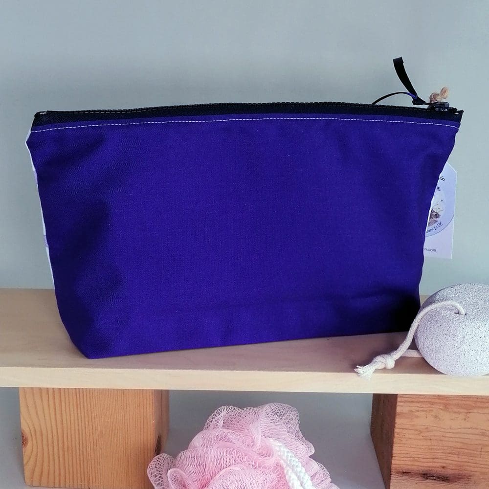 The back of the toiletries bag for the little running dog with a pink flower in it's mouth, is a deep purple cotton and has a chunky plastic zip fastener.