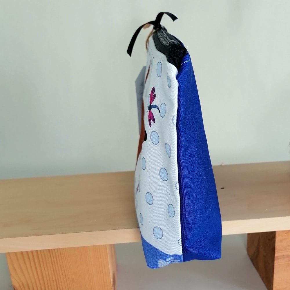The spotty blue front and the bright blue back can be clearly seen on the side view of the little brown dog toiletries bag