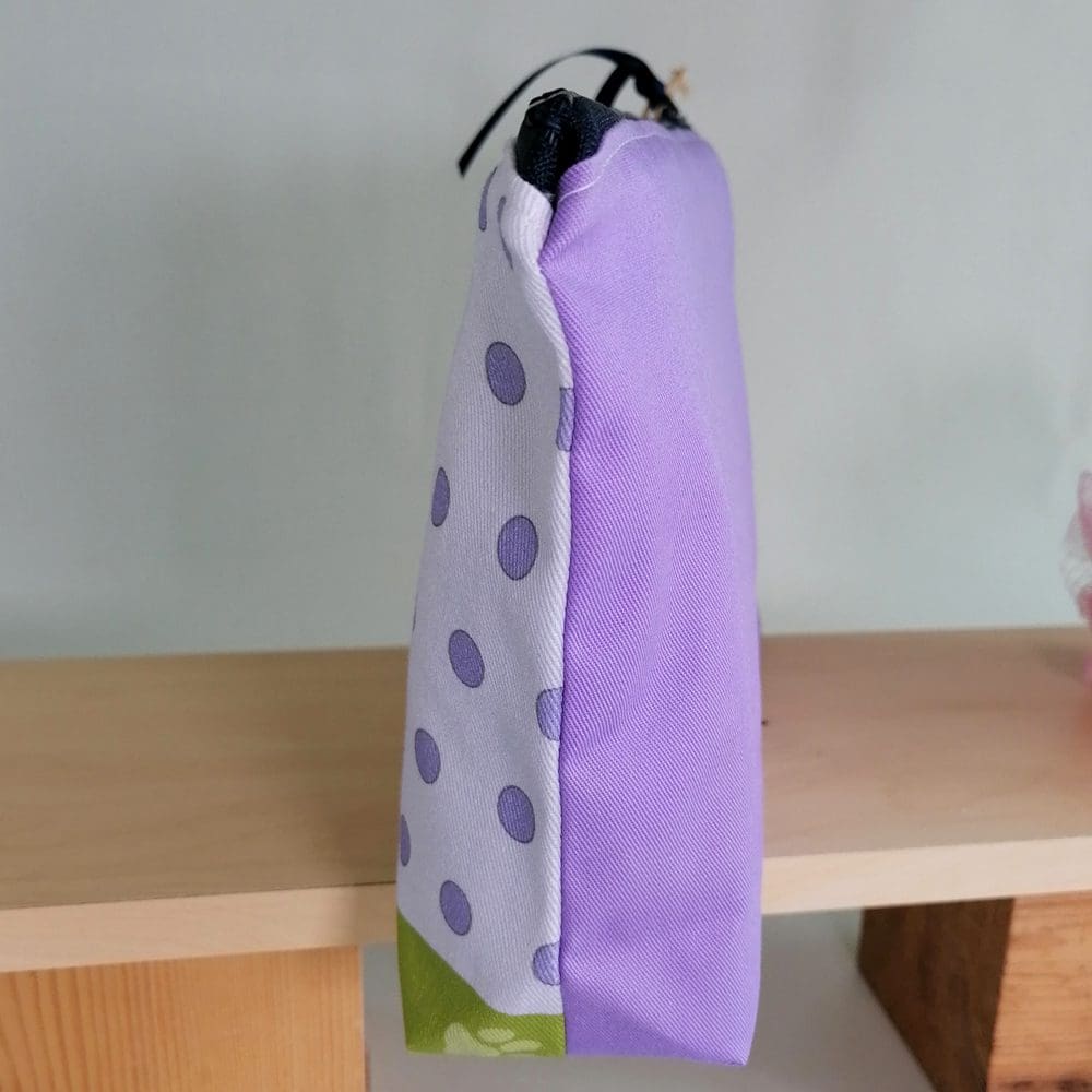 The spotty pale purple front and the rich purple back can be clearly seen on the side view of the little brown dog in a green bandana toiletries bag