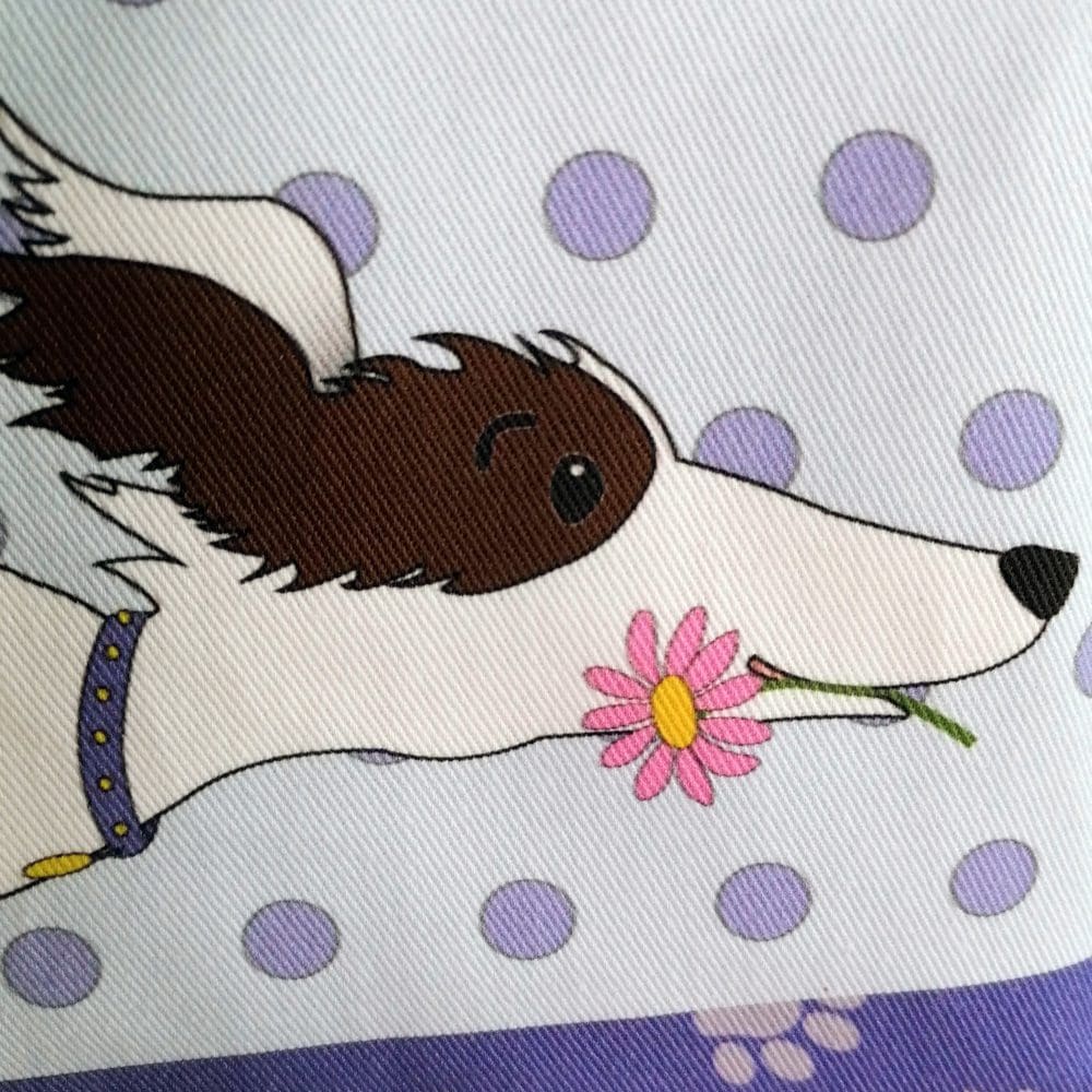 Heavyweight cotton fabric printed in vibrant colours detailing the head of the little running dog sporting a purple collar and carrying a pink flower in it's mouth
