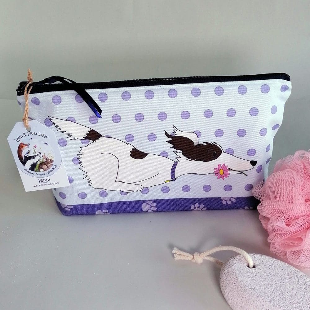 A large cotton handmade washbag featuring a background of pale purple spots, paw prints on the base and a brown and white scruffy dog wearing a purple collar running across the front of the bag with a pink flower in it's mouth.