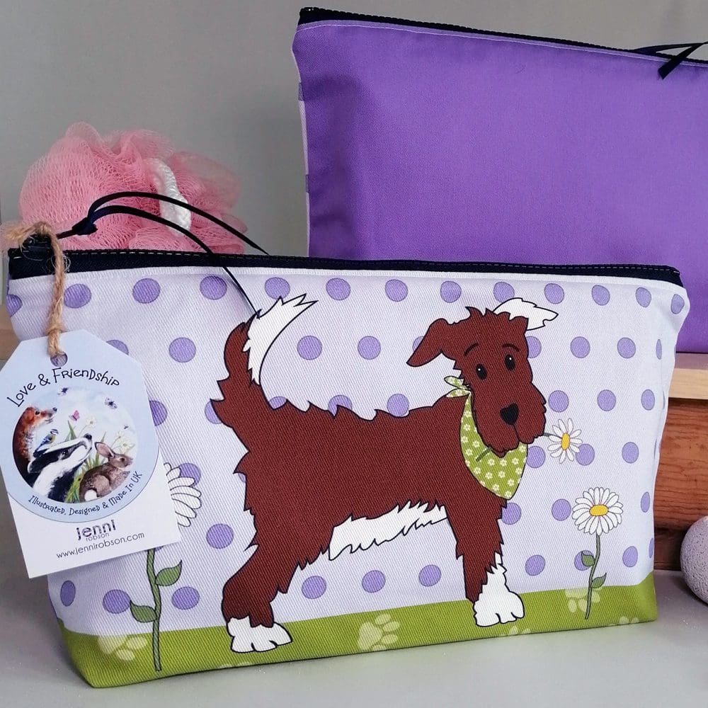 Two toiletries bags displaying both sides of the bag: the cheeky brown dog wearing a flowery green bandana on a spotty background on one bag and the rich purple back on the second bag.