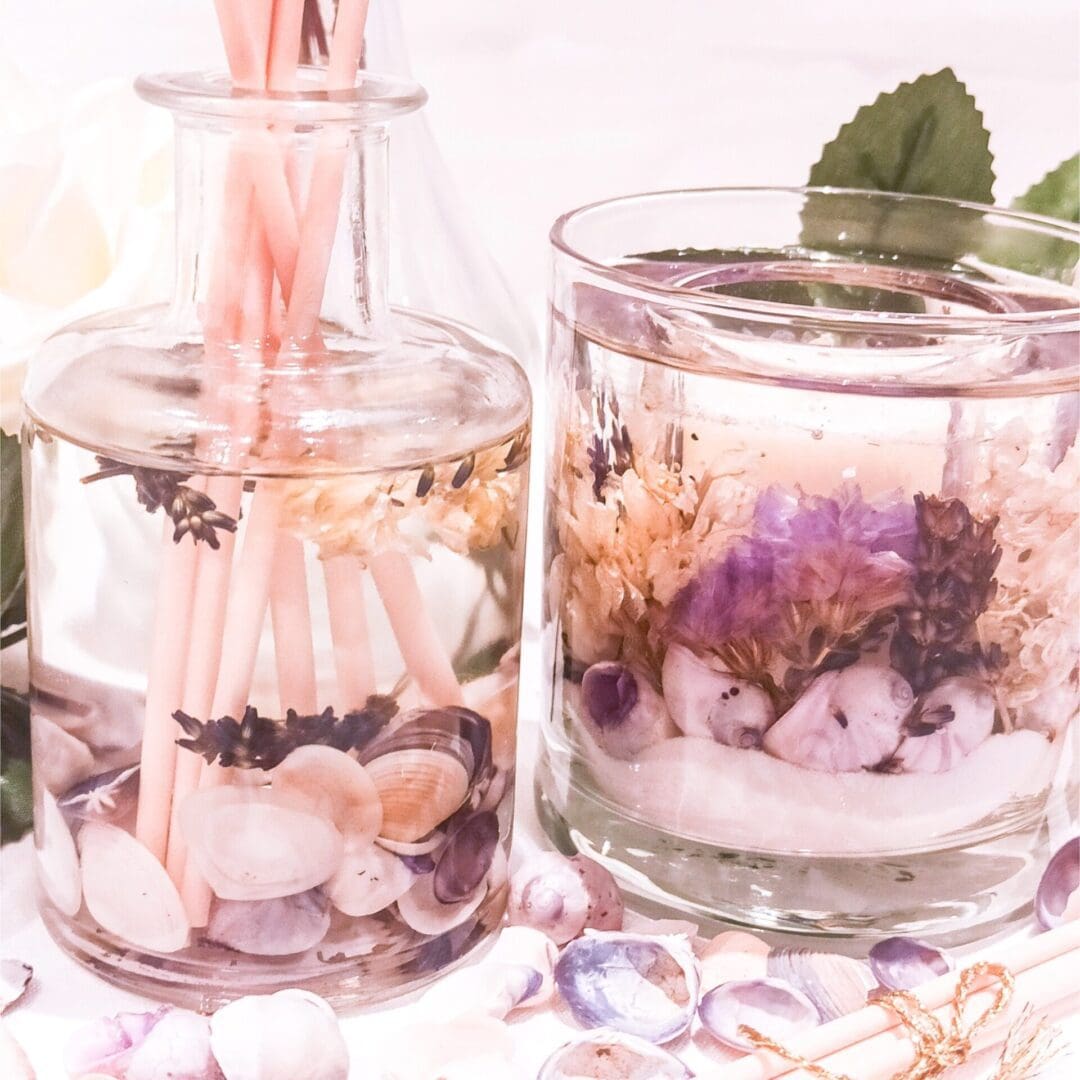 Lavender scented luxury botanical reed diffuser and candle on a table surrounded by shells and purple flowers